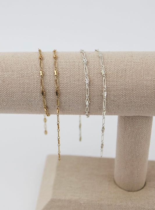 Gold filled and sterling silver chain bracelets displayed on a neutral fabric jewelry stand.