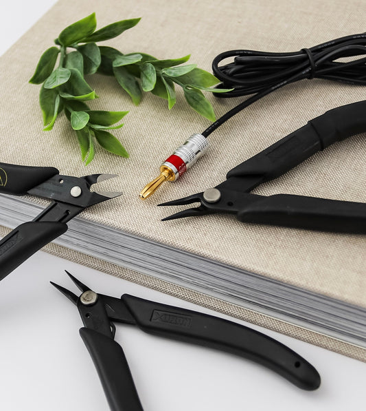 Permanent jewelry tools laid out on a work surface, including precision cutters, jewelry pliers, and a welding cable used for permanent jewelry applications.