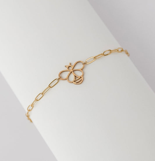 Delicate gold-filled bracelet featuring a cutout bee charm on an elongated cable chain, displayed on a white cylindrical stand.