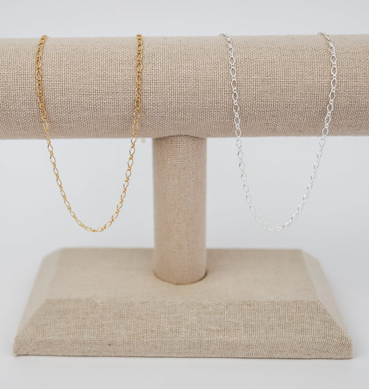 Gold and silver chain necklaces displayed on a beige linen jewelry stand.