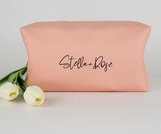 Peach-colored cosmetic pouch with the Stella + Rose logo, placed beside two white tulip flowers on a light background.