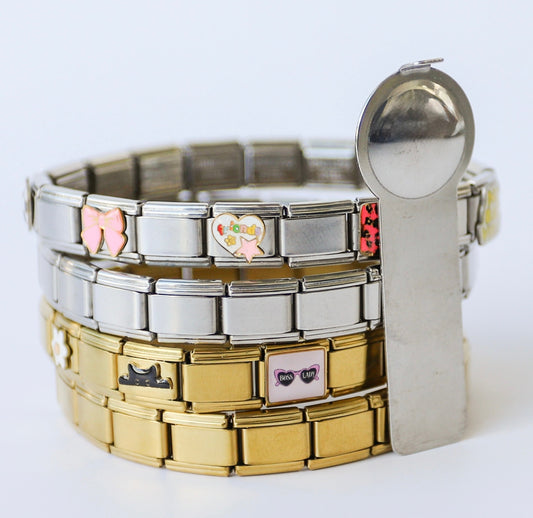 Stacked gold and silver Italian charm bracelets featuring various modular links with enamel designs, including a butterfly and a heart, set against a plain white background.
